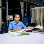 Trabalhadora de uma fábrica têxtil consulta documentos em uma mesa dentro da unidade industrial.