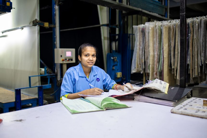 Trabalhadora de uma fábrica têxtil consulta documentos em uma mesa dentro da unidade industrial.