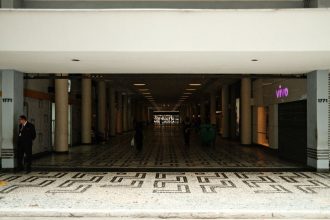 Corredor amplo de um shopping center moderno, com pessoas caminhando entre áreas comerciais.