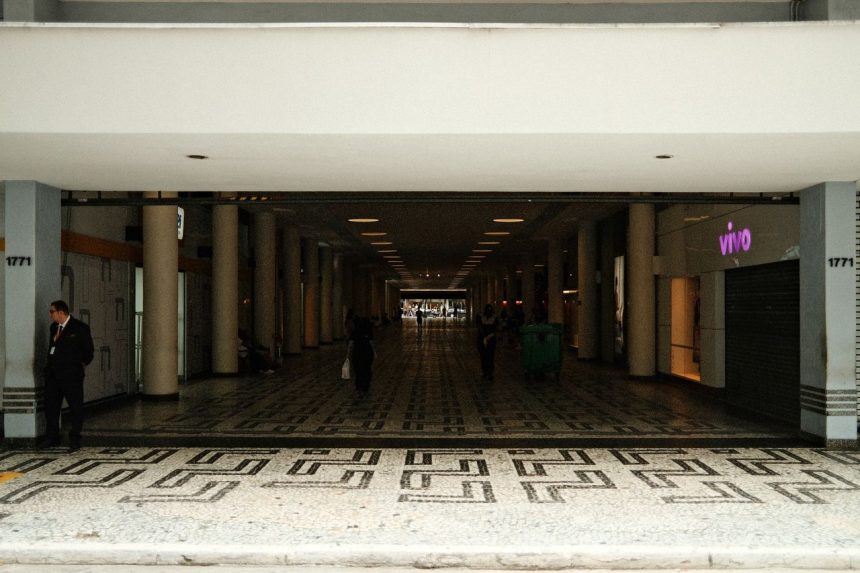 Corredor amplo de um shopping center moderno, com pessoas caminhando entre áreas comerciais.