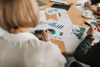 Profissionais analisam gráficos financeiros e usam calculadoras durante uma reunião de planejamento em um escritório.