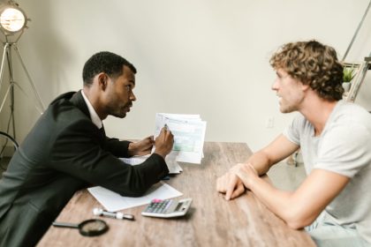 Profissional financeiro conversa com cliente enquanto analisa documentos em uma mesa de escritório.
